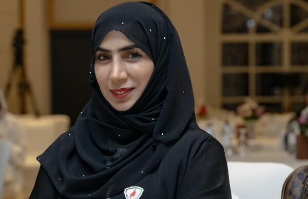 Dr. Aysha Ibrahim Al Dhaheri stands confidently in a well-lit room, dressed professionally. She holds a certificate in her hand, symbolizing her academic achievements and commitment to education. The background features a bookshelf with neatly arranged books, signifying knowledge and expertise. A subtle smile on her face reflects her positive and empowering personality. The image exudes professionalism and determination, capturing Dr. Aysha's inspiring presence.